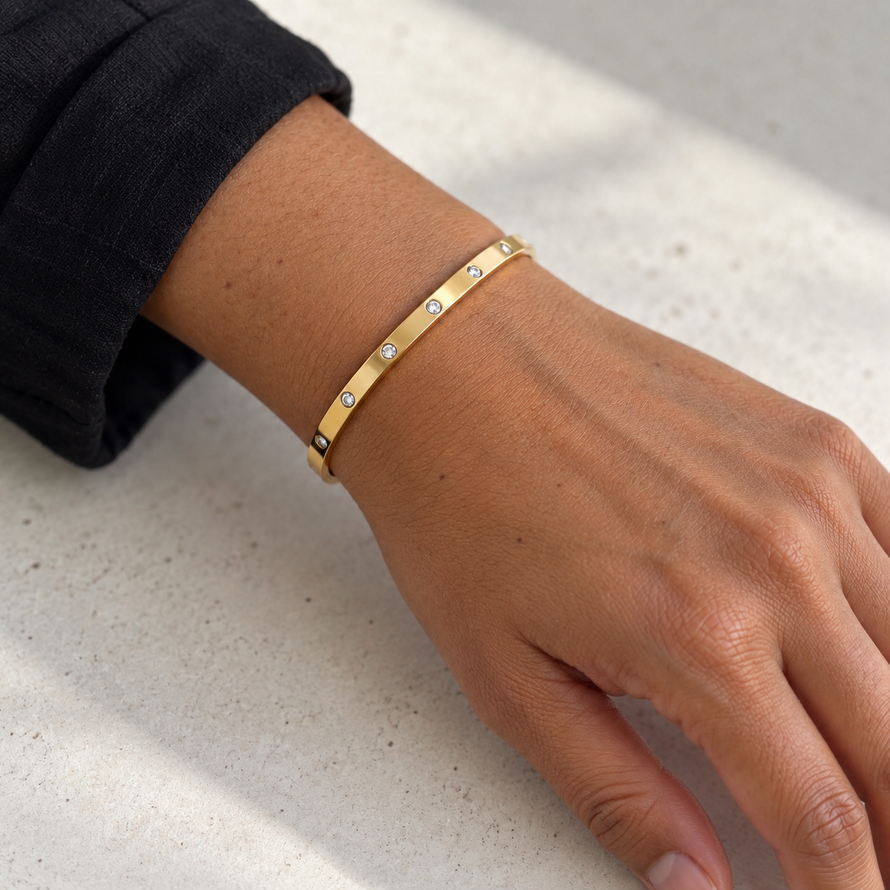 Brazalete Destello dorado de banda fina en muñeca femenina morena apoyada sobre una superficie clara
