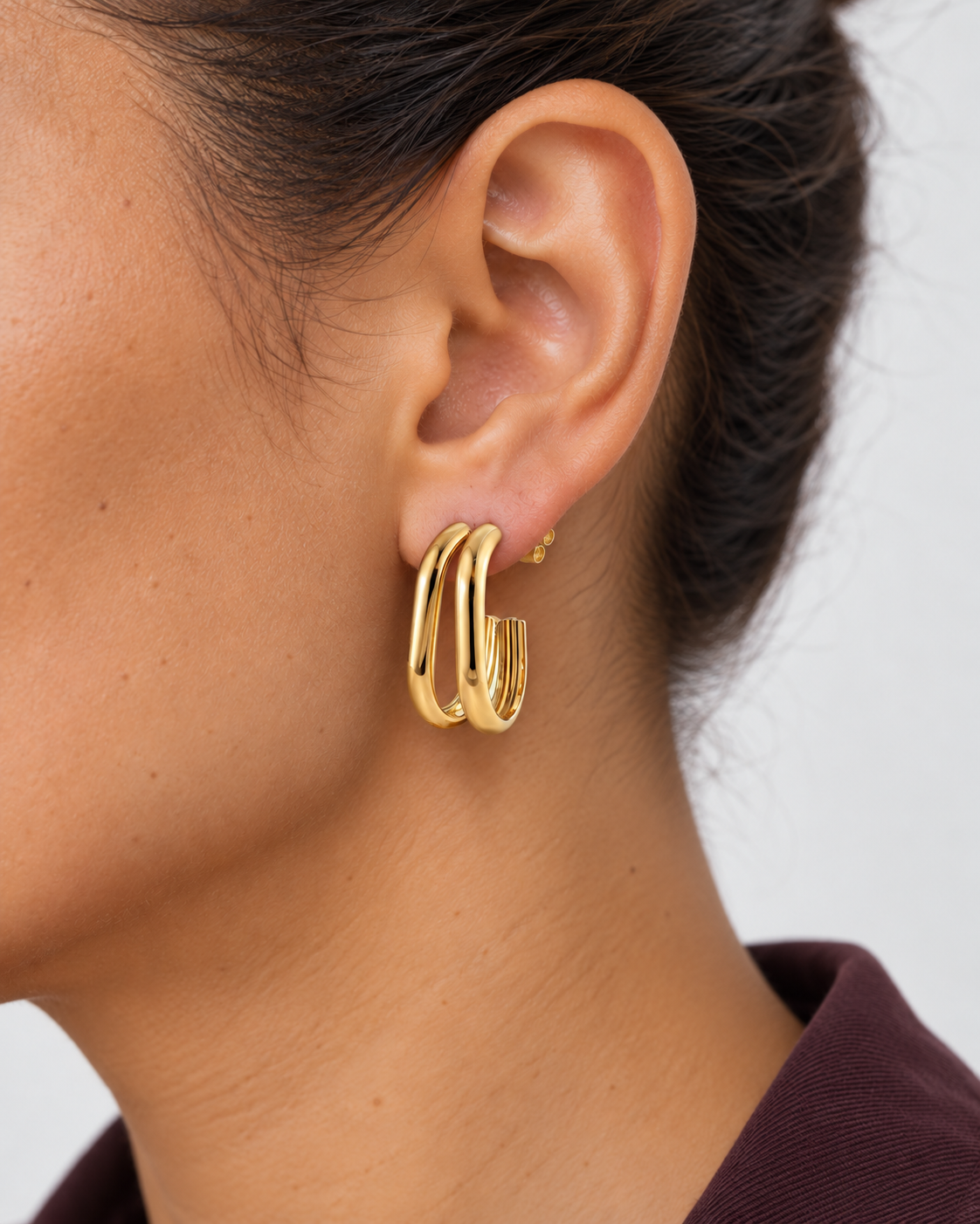 Pendiente Aparte dorado de unos 3 cm en oreja, con tuerca a presión puesta detrás del lóbulo