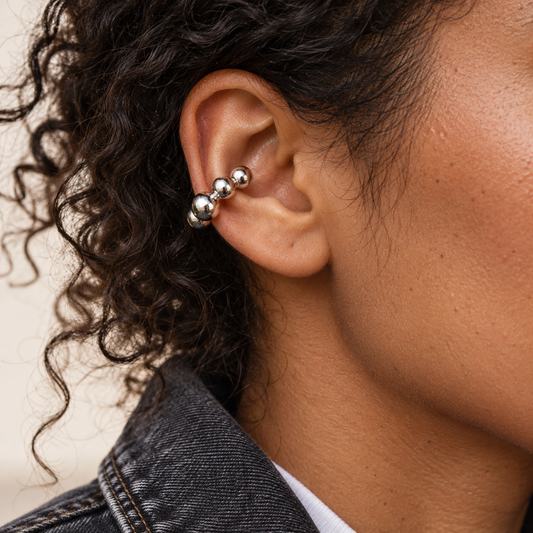 Earcuff Maii plateado de esferas en oreja, con piel natural y look de denim oscuro.