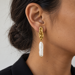 Pendiente Perla Brava dorado con perla alargada de 6 cm en una oreja morena