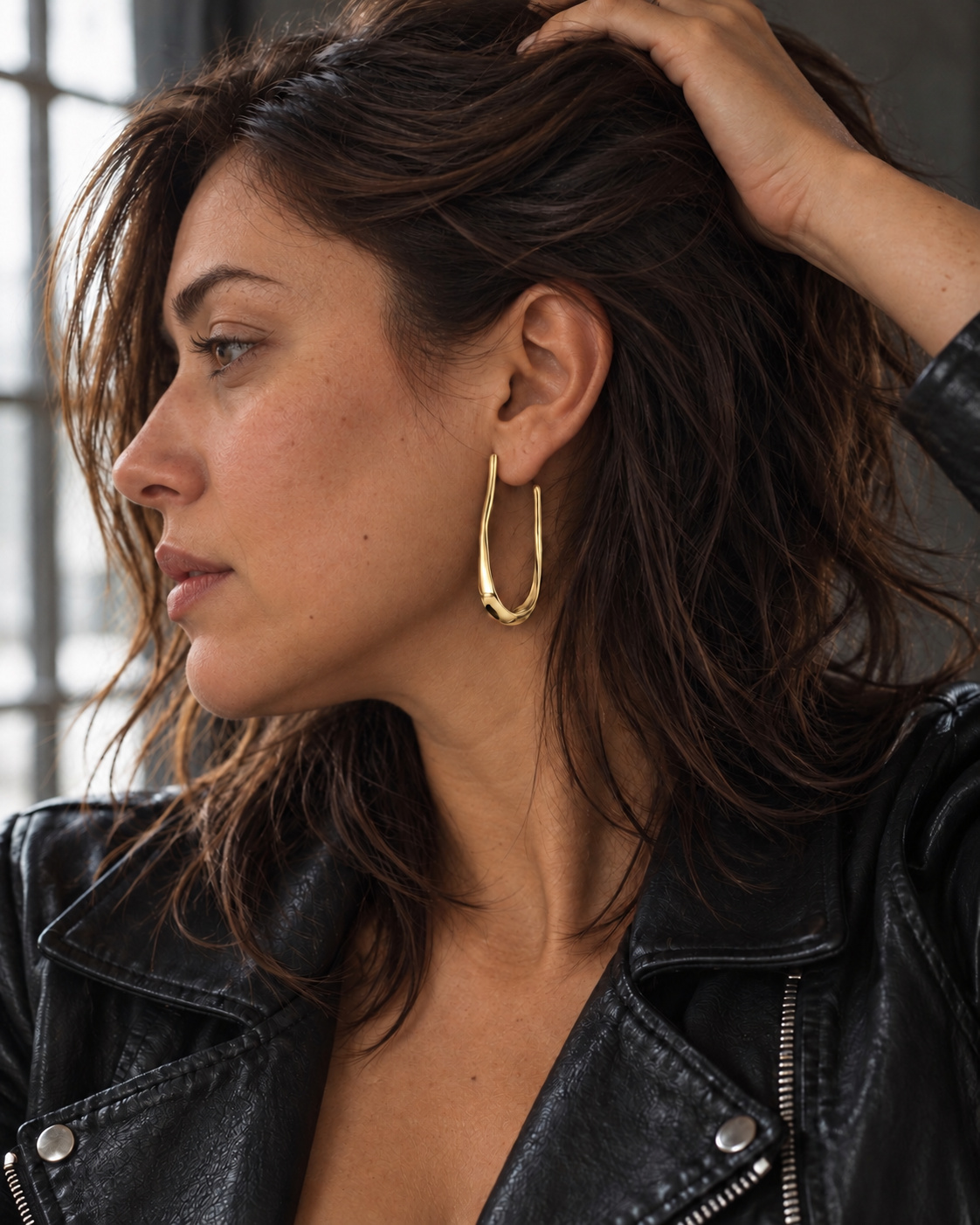 Pendientes Trazo dorados de 5 cm puestos en oreja, con chaqueta negra y luz natural